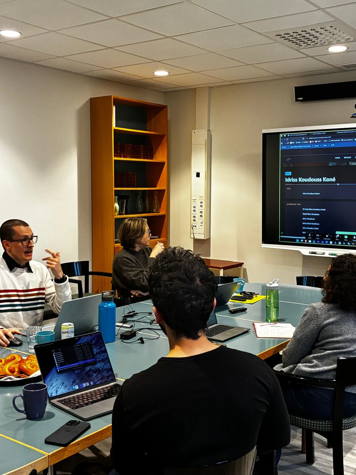 Frédérick Madore presenting to the ALMEDA team at Uppsala University around a conference table with laptops and a screen displaying research data