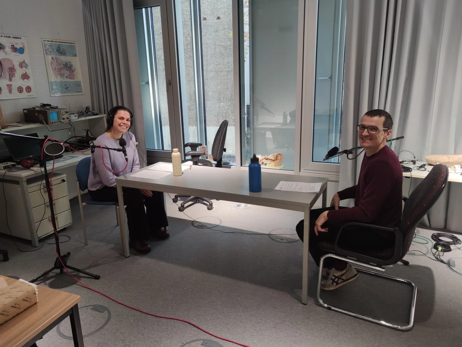 Frédérick Madore and Elisa Nobel-Dilaty sitting at a table with microphones and headphones in a recording studio for the ZMO Kitchen Talks podcast.